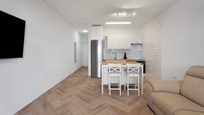 A modern kitchen with white cabinets, a stainless steel refrigerator, and a wooden island with two white bar stools.