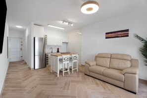 Una cocina moderna con armarios blancos, un refrigerador de acero inoxidable y una mesa de comedor de madera con sillas blancas.