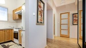 A kitchen with wooden cabinets, a stove, and a refrigerator. There is a hallway with wooden doors and a mirror. - Powiśle 2-Bedroom Apartment (Warszawa)