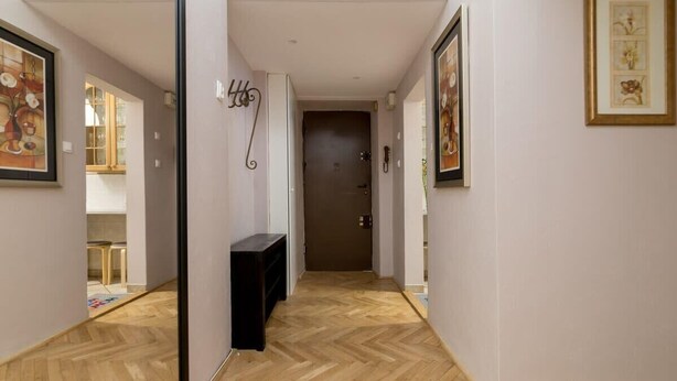 A hallway with a wooden herringbone floor, a door at the end, and framed artwork on the walls. - Powiśle 2-Bedroom Apartment (Warszawa)