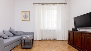 A living room with a grey sofa, a small table with cups, a TV on a wooden cabinet, and sheer white curtains. - Powiśle 2-Bedroom Apartment (Warszawa)