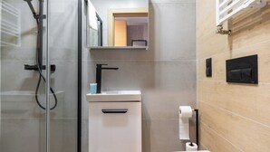 A modern bathroom with a glass shower enclosure, a white toilet, and a wooden vanity with a mirror. - Reymonta 24 Studio with FREE PARKING (Katowice)