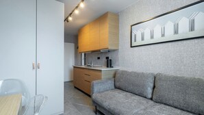 A modern kitchen with wooden cabinets, a grey sofa, and a framed picture on the wall. - Reymonta 24 Studio with FREE PARKING (Katowice)
