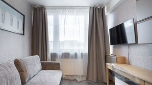 A modern living room with a sofa, a TV mounted on the wall, and a window with curtains. - Reymonta 24 Studio with FREE PARKING (Katowice)