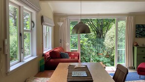 A dining area with a wooden table, bench seating, and a view of greenery outside. - Light-Filled Hira Home (Hira)