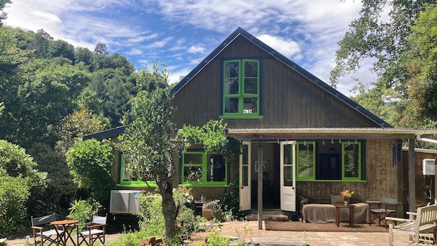 A wooden house with a porch, green-framed windows, and a brick patio. - Light-Filled Hira Home (Hira)