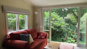 A cozy living room with a red sofa, a wooden coffee table, and a view of lush greenery through large windows. - Light-Filled Hira Home (Hira)