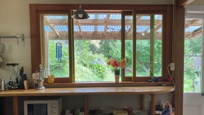A kitchen with a built-in microwave, shelves with dishes, a blender, and a window with a view of greenery. - Light-Filled Hira Home (Hira)