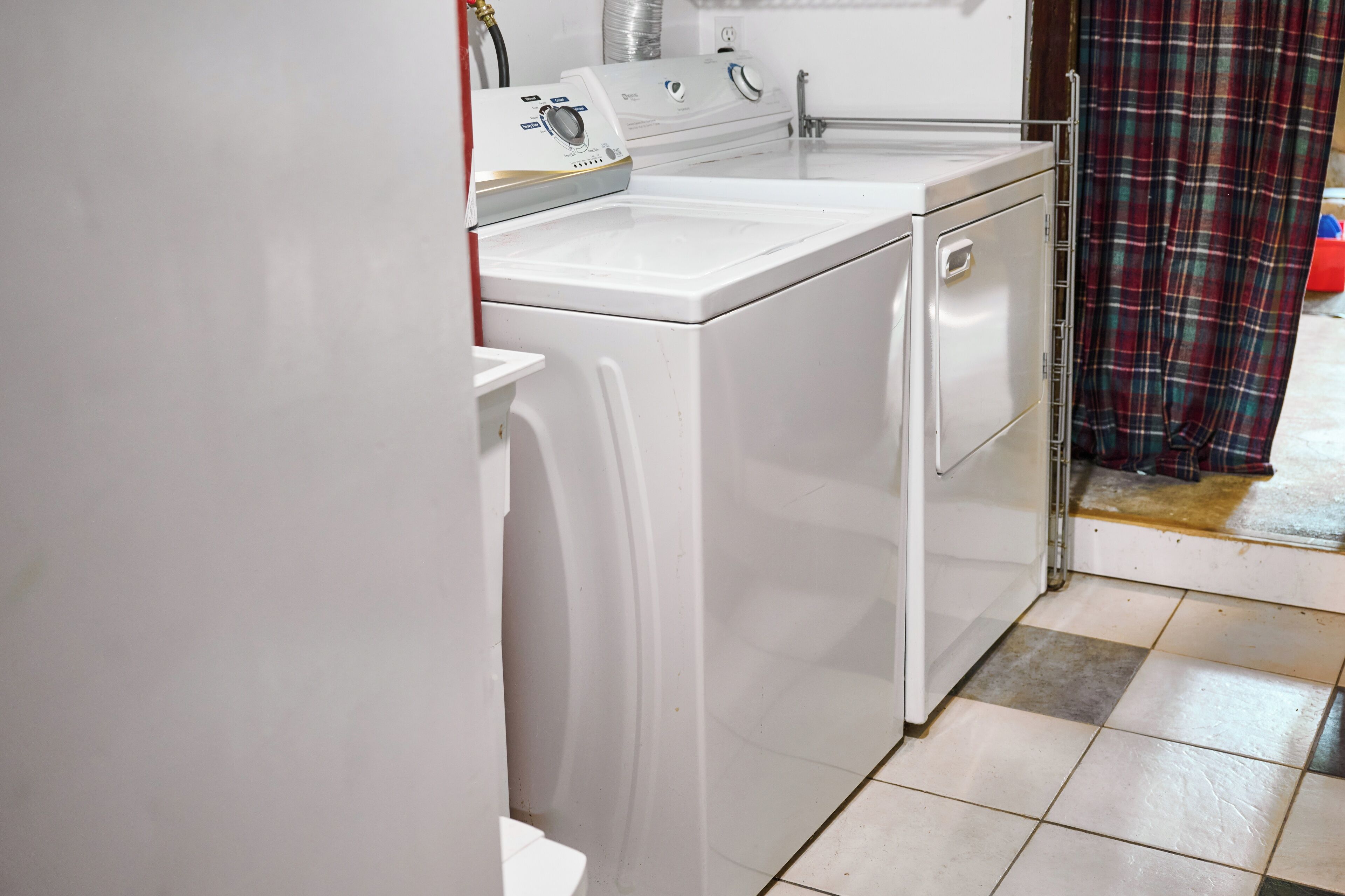A laundry area with a front-loading washing machine and dryer, a tiled floor, and a plaid curtain.