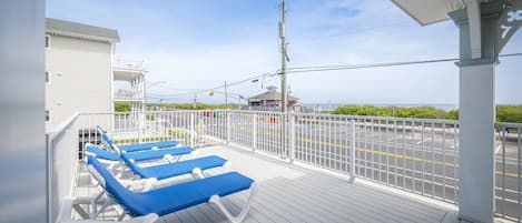 A deck with blue lounge chairs, a white railing, and a view of the road and greenery.