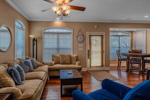 A living room with a sofa, coffee table, and blue chair; a dining area with a table and chairs; and a ceiling fan.