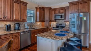 A kitchen with wooden cabinets, granite countertops, stainless steel appliances, and a central island with blue placemats. - Ocean Lakes T36 (Myrtle Beach)