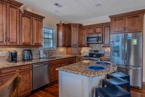 A kitchen with wooden cabinets, granite countertops, stainless steel appliances, and a central island with blue placemats.