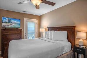 A hotel room with a bed, a TV, a ceiling fan, a nightstand, and a door leading to a balcony.
