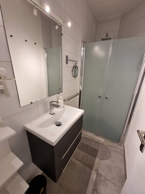A modern bathroom with a white sink, dark vanity, a large mirror, and a glass shower enclosure. - Superb apartment completely renovated 4EST211 (LE BARCARES)