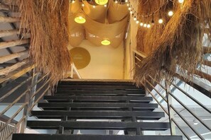 Un escalier au design moderne, doté d’une rampe en métal et d’un plafond orné de luminaires suspendus.
