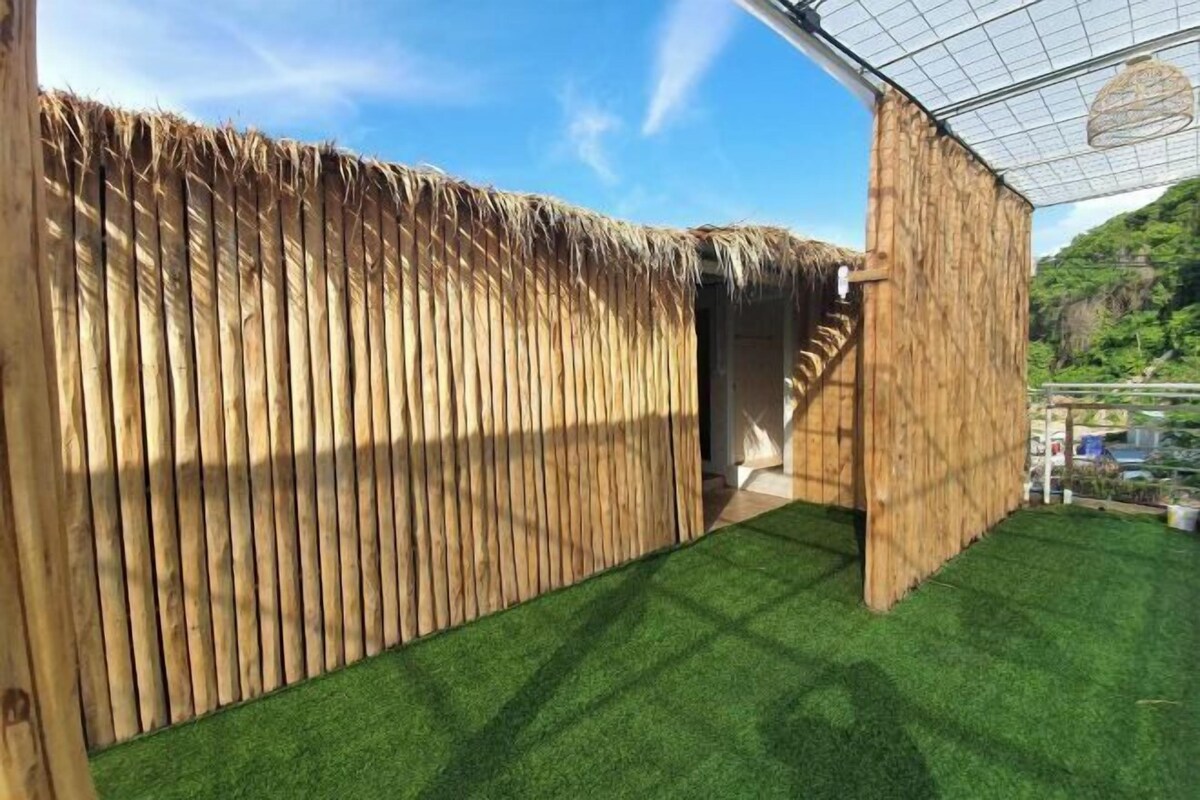 Une structure en bois avec un toit de chaume, une petite entrée et une pelouse artificielle verte.