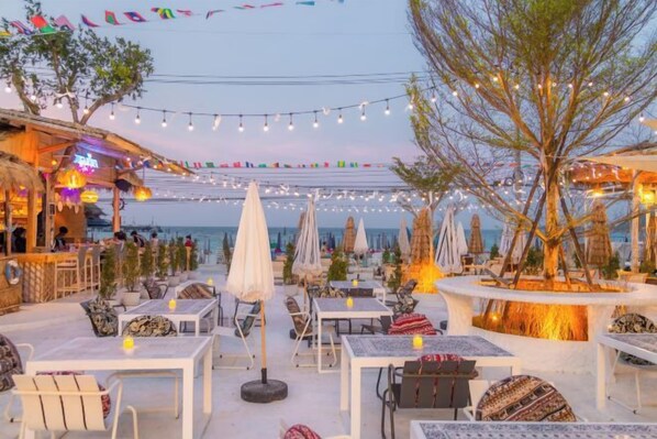 An outdoor seating area with tables and chairs, string lights, and umbrellas.