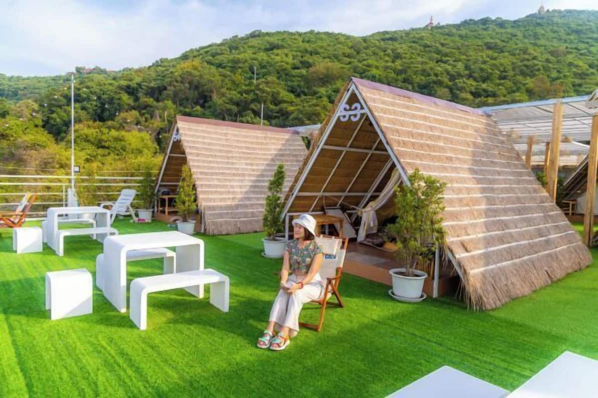 Un espace extérieur moderne aménagé avec des meubles blancs et une structure surmontée d’un toit de chaume.