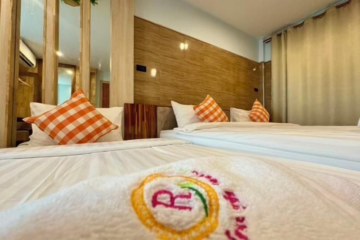 Una habitación de hotel con dos camas, almohadas a cuadros, cabecero de madera y un logotipo visible en la colcha.