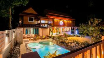 A two-story building with a swimming pool, outdoor seating, and a well-lit entrance.
