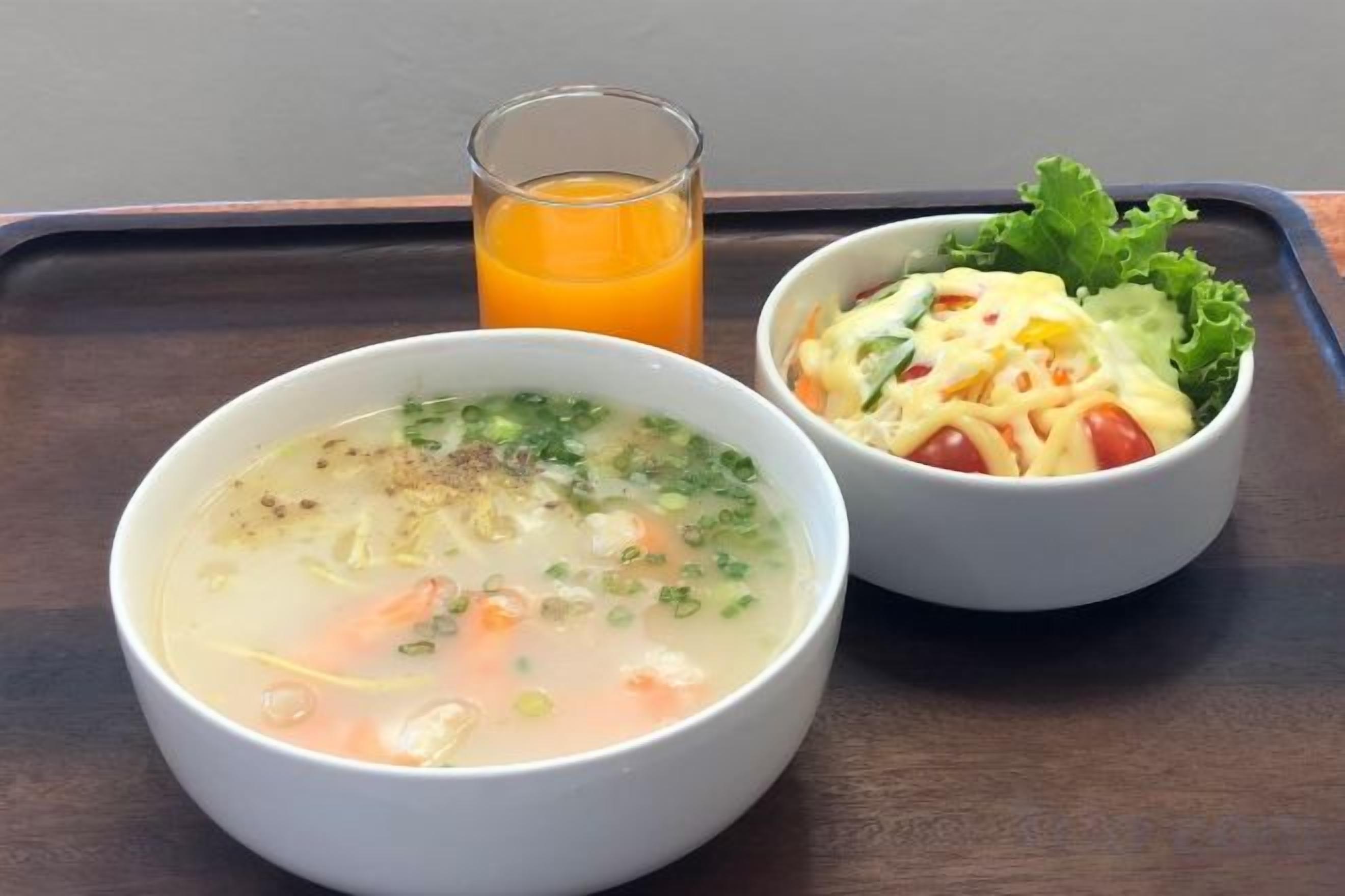 Deux bols de nourriture sur un plateau, l’un contenant une soupe et l’autre une salade, ainsi qu’un verre de jus d’orange.