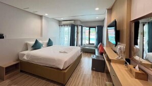 A hotel room with a bed, a TV, a desk, and a window with curtains.