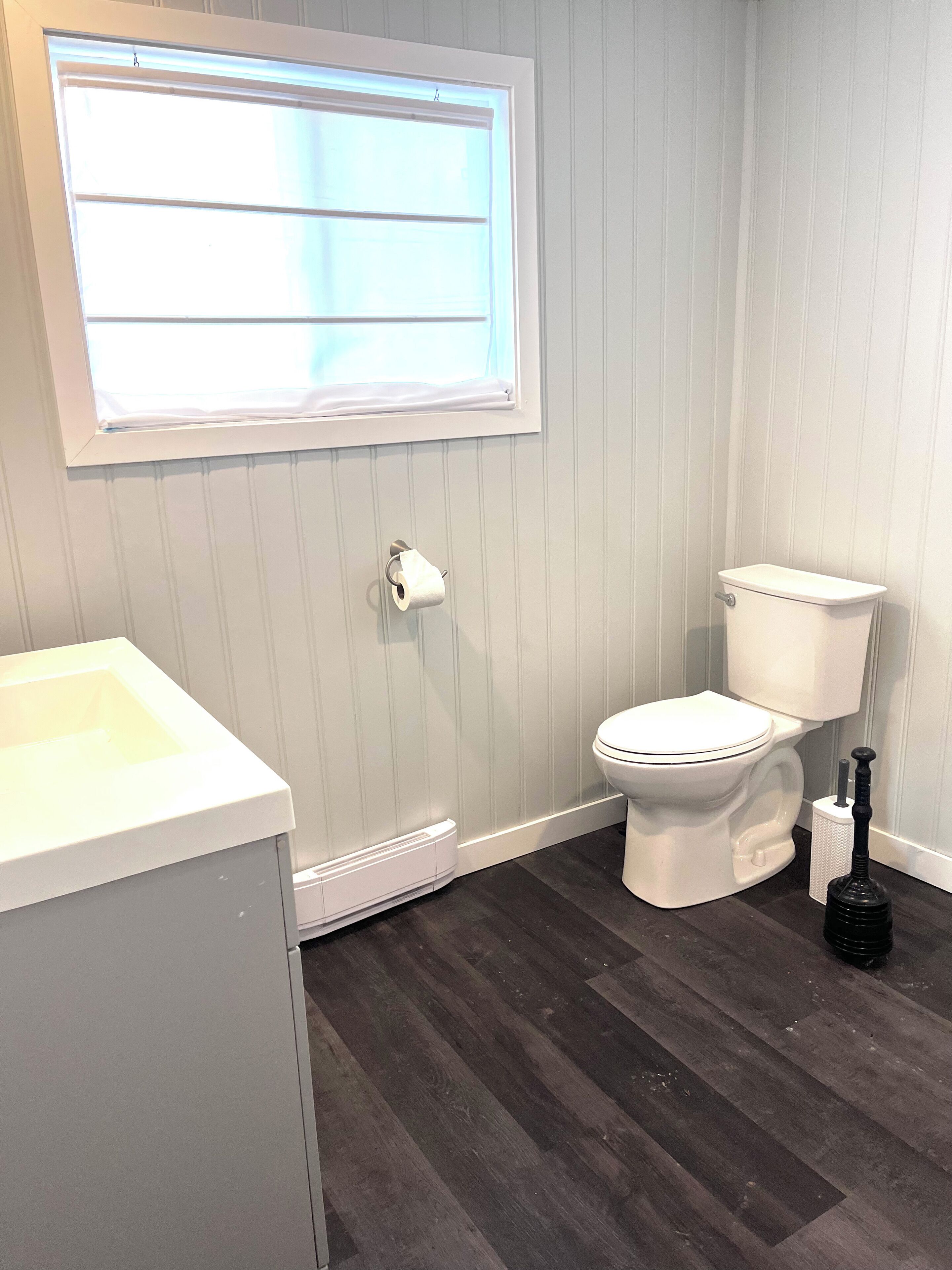 Een badkamer met een toilet, een raam, een wastafel en een ontstopper.