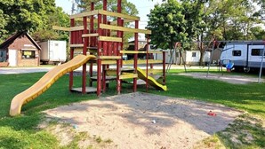 A playground with a slide and climbing structure, surrounded by grass and trees.