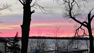 A dock with a view of a sunset over a body of water, surrounded by leafless trees.