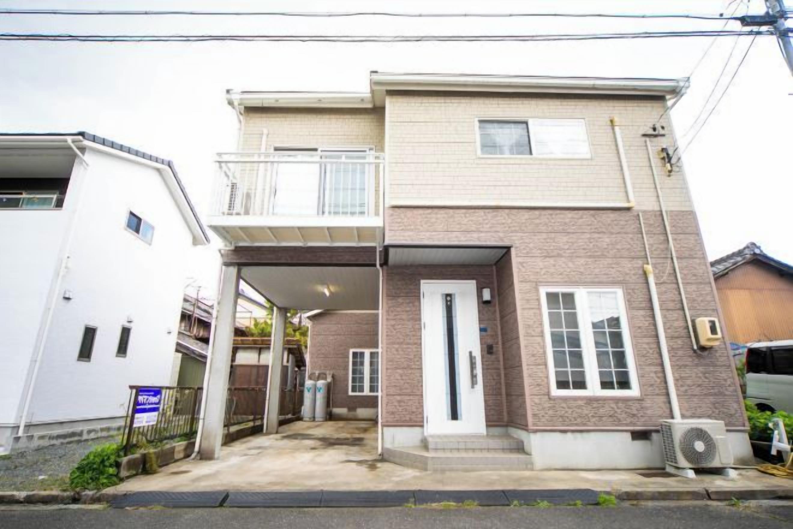 A two-story residential building with a covered entrance, a balcony on the upper floor, and a small attached garage.
