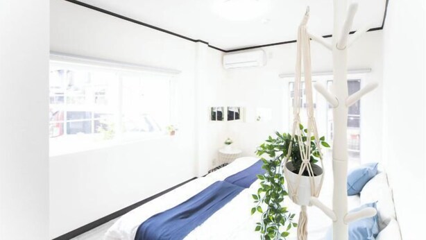 Una habitación luminosa y blanca con una cama, una planta colgante y una silla blanca.
