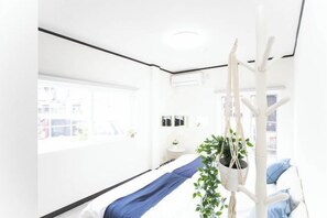 Une pièce lumineuse et blanche, avec un lit, une plante suspendue et une chaise blanche.