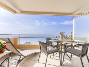 En balkon med et spisebord, fletstole, en vase med blomster og en flaske vin.