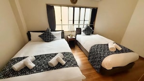 Quarto de hotel com duas camas, uma mesa de cabeceira, uma luminária e uma janela com cortinas.