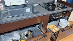 Uma cozinha compacta com fogão a gás, pia e forno embutido. Há armários com gavetas e uma pequena área de bancada.