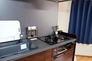 A compact kitchen with a gas stove, a sink, and a small countertop area. - Japanese cottage Han (Osaka)