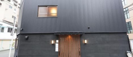A modern two-story building with a dark exterior, a wooden door, and a small window.