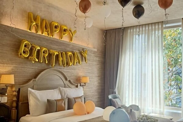 Una habitación de hotel con una cama, una decoración de globos con la inscripción 'HAPPY BIRTHDAY' y una ventana con cortinas.