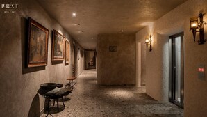 A hallway with framed pictures on the walls, a table with a pot and a bowl, and a door with a light fixture. - Le Recit Boutique Hotel De Dalat (Xuan Huong - Da Lat)