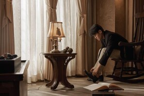 Una habitación con una mesa de madera, una lámpara, una mecedora y un libro abierto en el suelo.