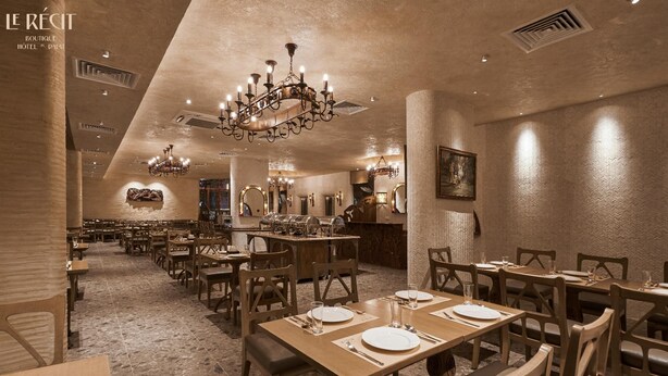 A restaurant with wooden tables and chairs, a chandelier, and a stone floor. - Le Recit Boutique Hotel De Dalat (Xuan Huong - Da Lat)