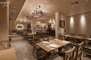 Ein Restaurant mit Holztischen und -stühlen, einer Kristallleuchter und einem Steinfußboden.
