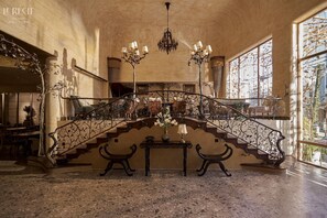 Un magnifique escalier, orné de rampes de métal ouvragées et surmonté d’un lustre, menant à un plafond très haut.