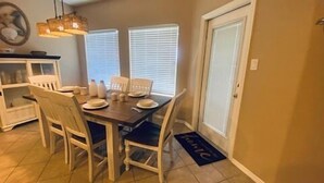 A dining area with a table set for four, surrounded by white chairs. - Chic Villa By The Bay- 48 TP (Laguna Vista)