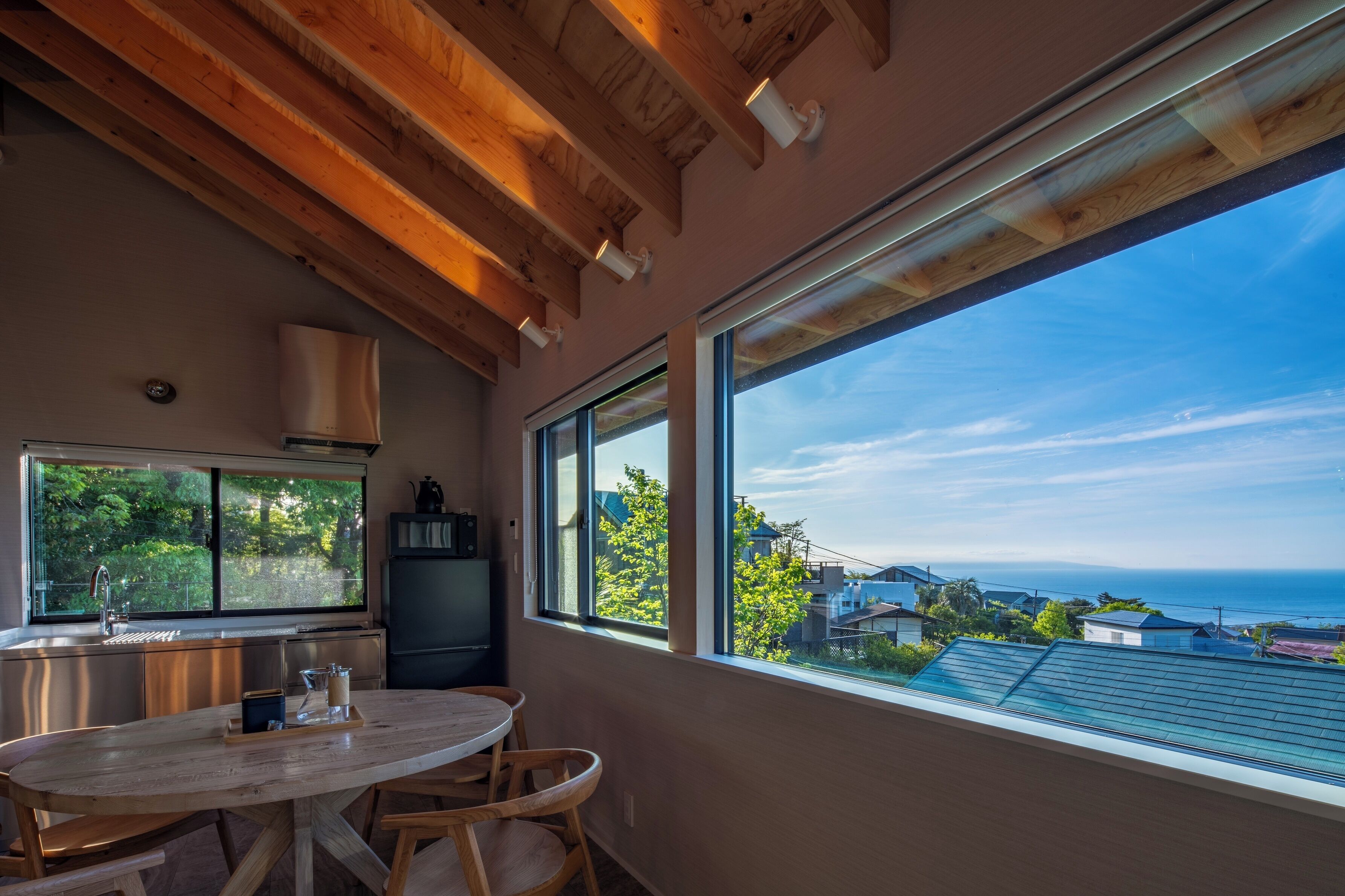 A modern kitchen with a large window, wooden ceiling beams, and a dining area with a table and chairs.