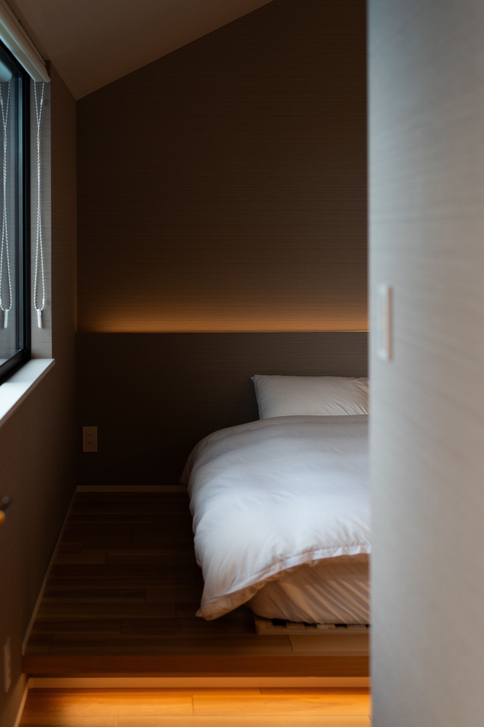 A bedroom with a bed, a window with curtains, and a wooden floor.