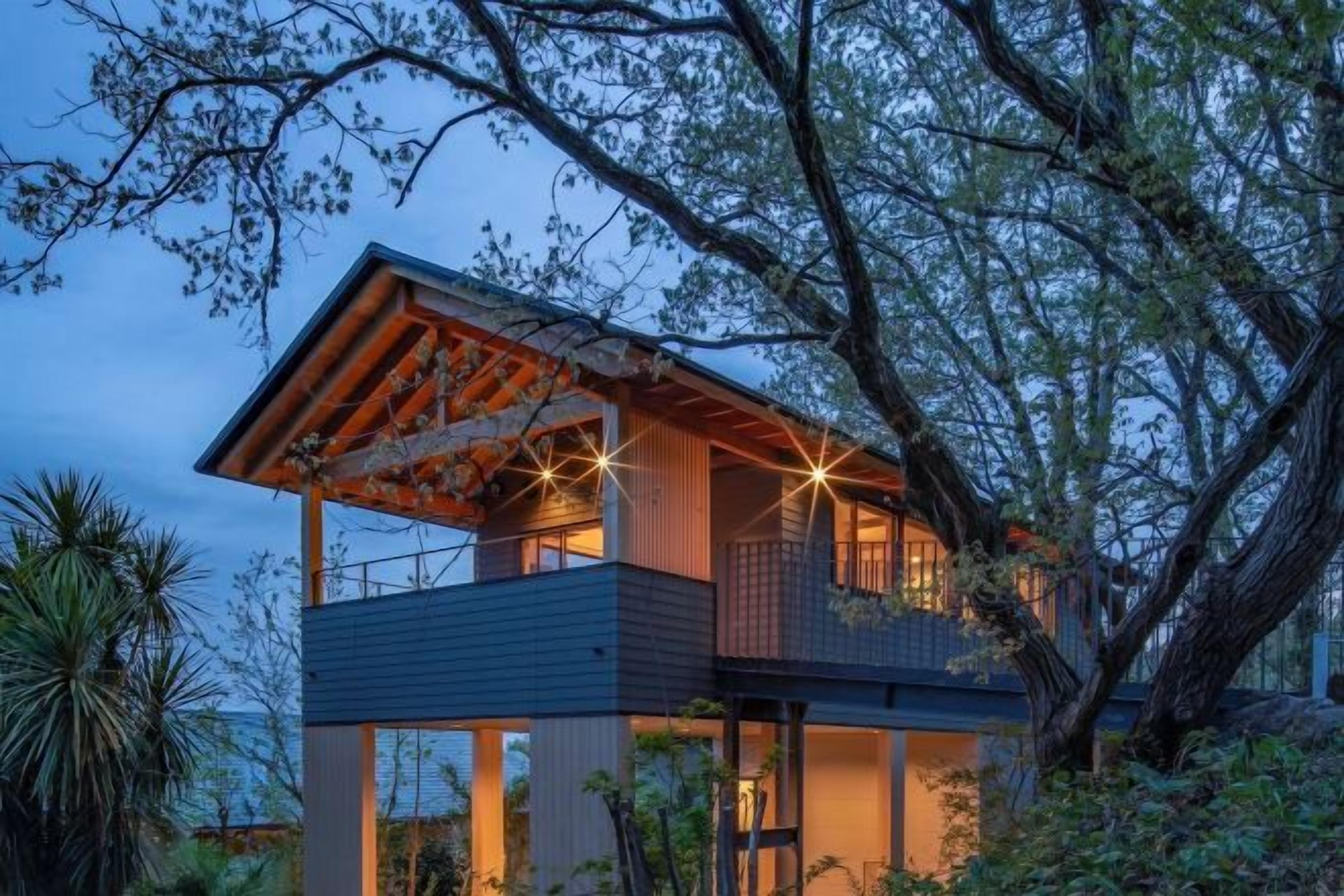 A modern two-story house with a balcony, surrounded by trees.