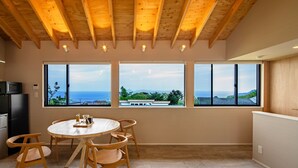 A modern kitchen with a dining area, large windows, and a view of the sea. - Nutic Izu (Ito)