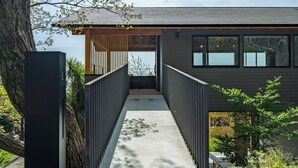 A modern building with a concrete pathway leading to a covered entrance, surrounded by trees and a clear sky. - Nutic Izu (Ito)